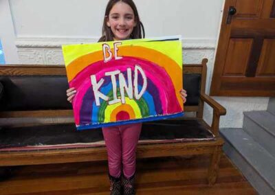 Child holds a sign with rainbow and Be Kind.